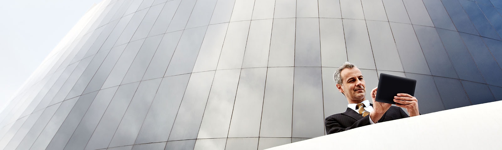 Person standing in front of a building and looking at a tablet.