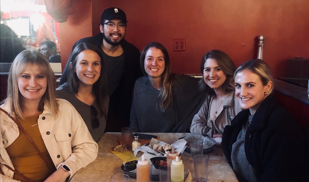 Six people huddle around a table and smile.