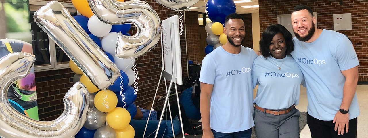 Three people stand together smiling and wearing shirts that read, “#OneOps.”