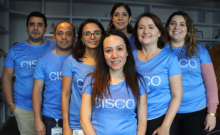 Seven people standing in a triangle formation smiling and wearing the same Cisco shirt.