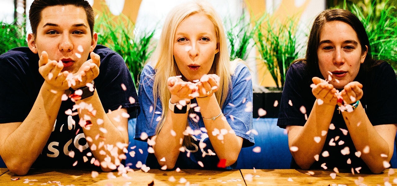 Male and two females blowing confetti from their palms in celebration from Cisco office in Raleigh, North Carolina