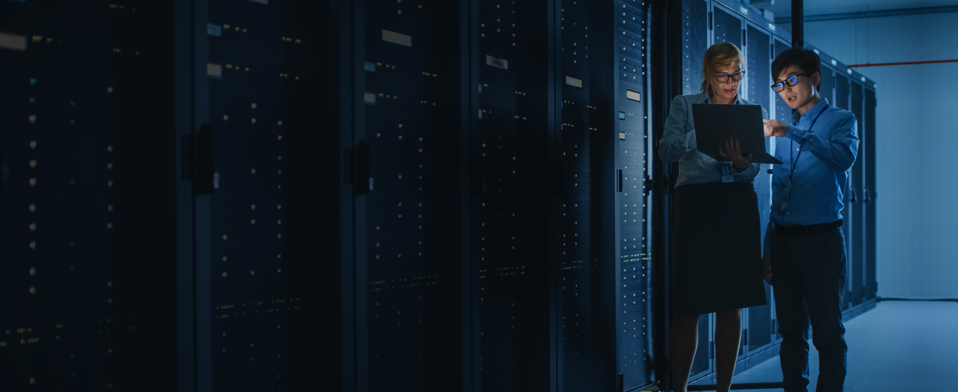 Two employees standing in a data center and reviewing a dashboard on a laptop