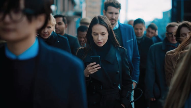 Eine Frau schaut in einer belebten Fußgängerzone auf ihr Mobiltelefon