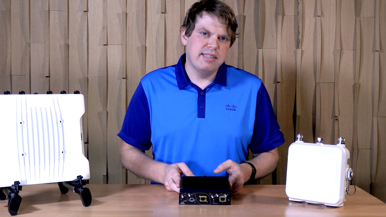 A person at a table displaying Catalyst IW9165E and two other Cisco access points.